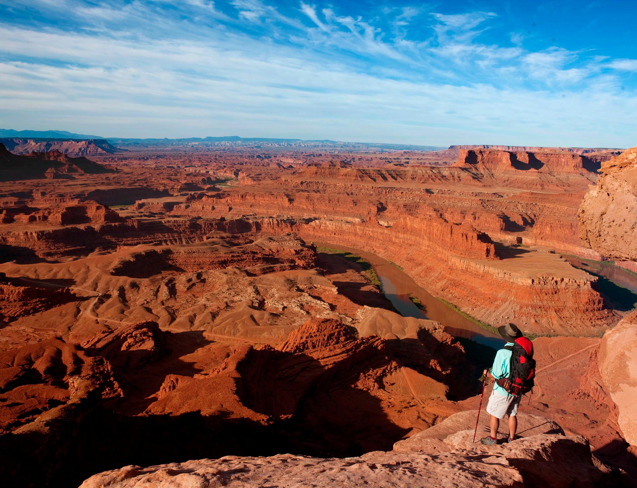 A person stands at the edge of a vast canyon with a river below.