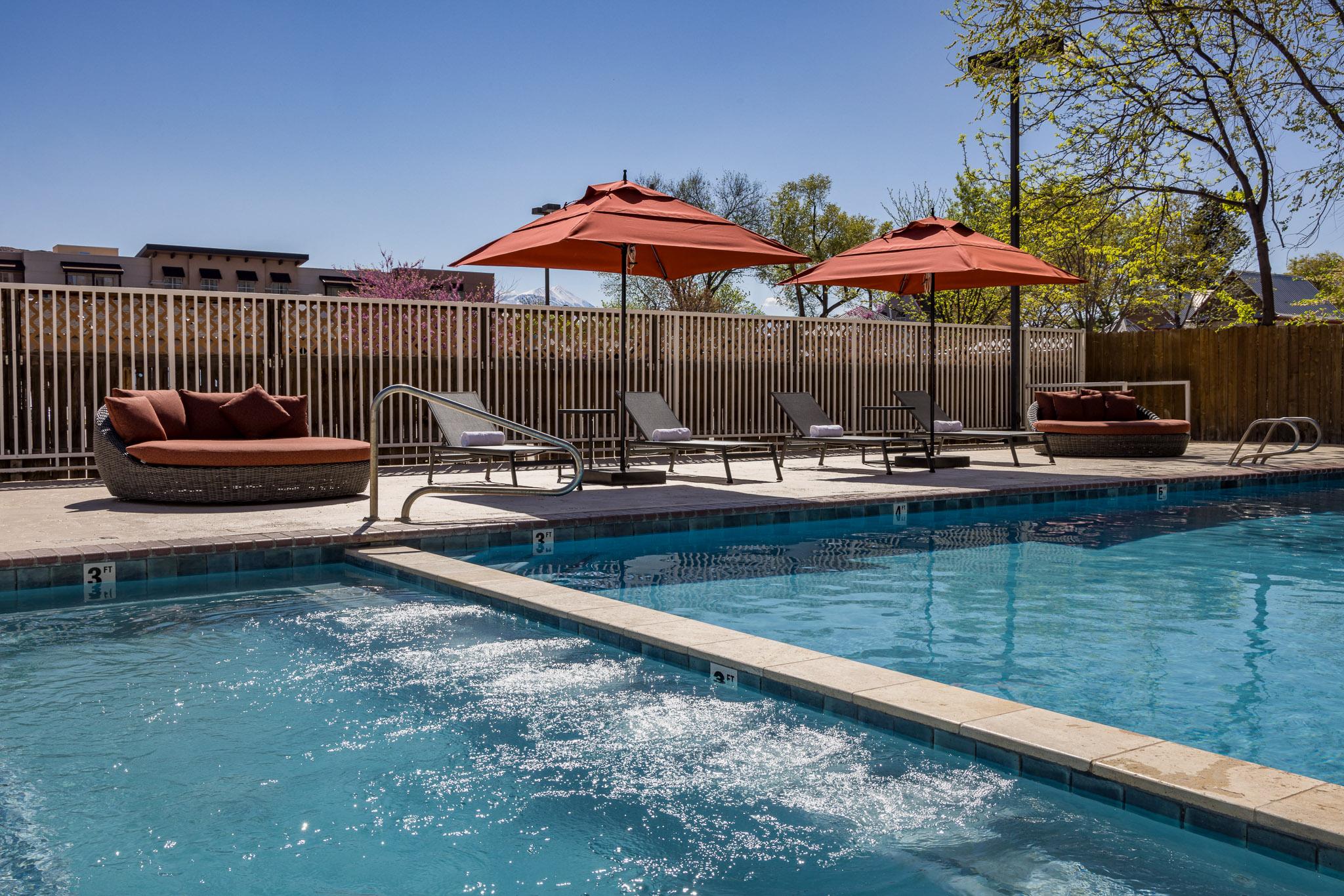 A swimming pool with a fountain, surrounded by lounge chairs and umbrellas.