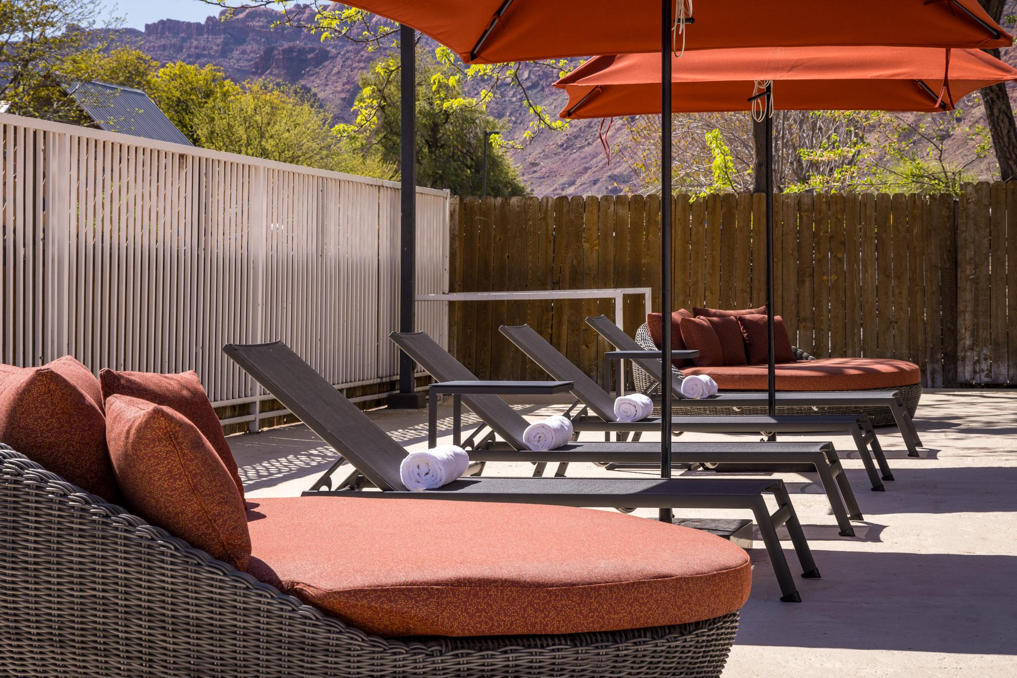 A poolside patio with lounge chairs, umbrellas, and a view of mountains.
